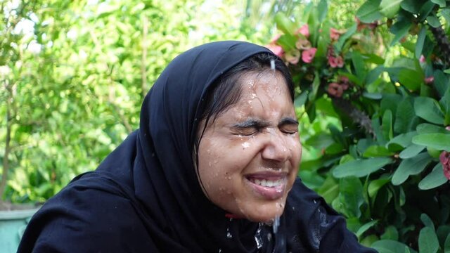 A woman splashes cold water on her face on a hot day. A Muslim woman dressed in black is performing ablution with water. The concept of cleaning the face with water. Slow-motion video. 