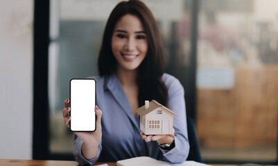 Real estate agent showing house model and mobile phone with blank white screen for advertisement