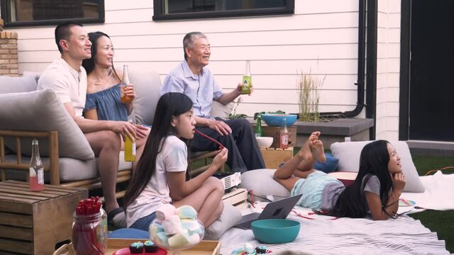 Multigenerational Family Watching Movie In Summer Backyard