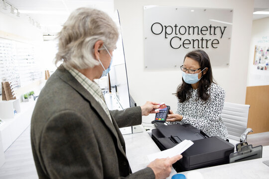 Patient in face mask paying receptionist in optometry center