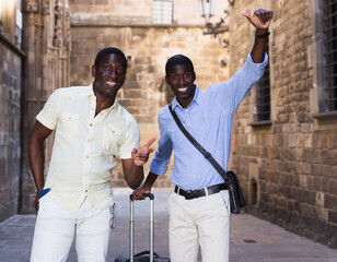 Naklejka na ściany i meble Portrait of smiling happy friends tourists with luggage on the street of old european city