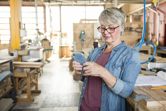 Senior female woodworker using smart phone in wood shop