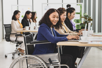 Asian business women including handicap woman sitting on wheelchair working hard on laptop on the table in office. Concept for business meeting