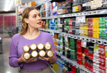 Focused positive female customer selecting beer in supermarket