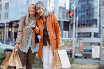 Pretty mature women with lot of shopping bags laugh on modern city street on autumn day. Friends...