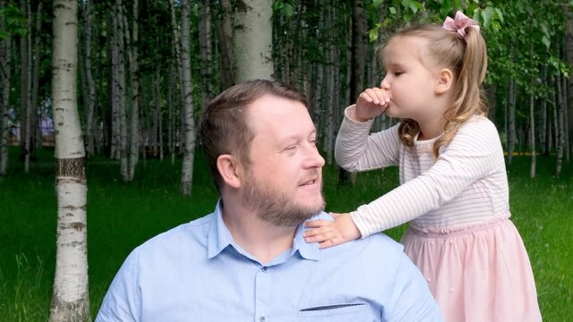 cheerful little daughter, 3 years old, tells her daddy in her ear and laughs. The concept of a happy childhood, fatherhood, parenting. A trusting relationship between parents and children. Fathers day