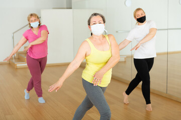 Fototapeta na wymiar Three mature European women in masks are dancing in fitness room