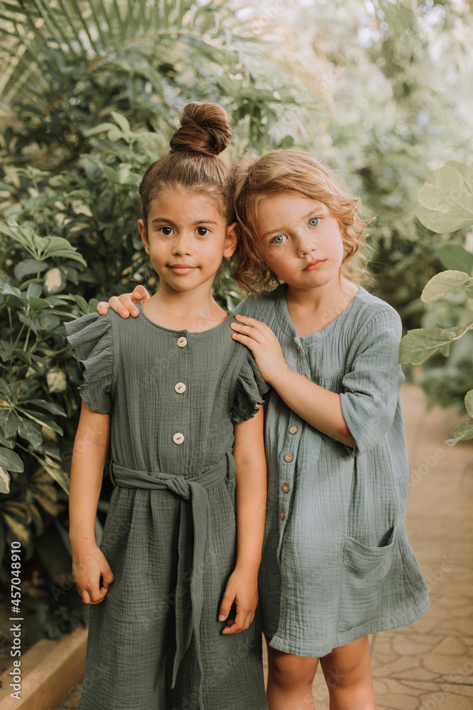 Wall mural portrait of two charming smiling girls belonging to different races surrounded by tropical leaves. f