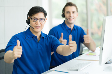 Handsome man in blue shirt customer service operator showing thumbs up while working with computer...