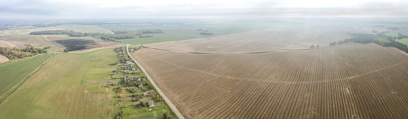 panoramic aerial view of countryside landscape with village among agricultural fields in the autumn morning mist