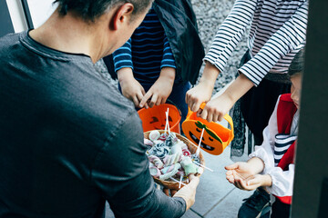 Close-up of a man handing out sweets to joyful children on Halloween. Children's tricks or treats....