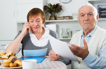 Elderly couple carefully consider contract before signing at table at home