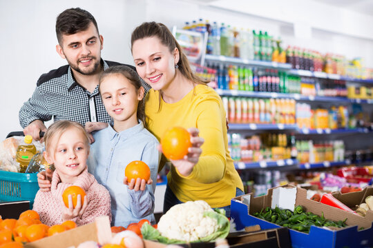 Happy cheerful positive family with two little girls looking for fresh oranges in supermarket