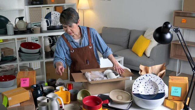 Mature Asian woman entrepreneur, Business owner working from home. Ceramic crockery product. packing package before shipping product to client.