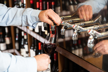 Hands of bartender pouring red wine from tap. High quality photo