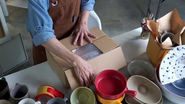Mature Asian woman entrepreneur, Business owner working from home. Ceramic crockery product. packing package before shipping product to client.