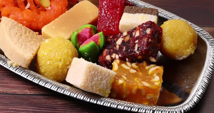 Colorful variety of Indian sweet desert jilepi jilapi amriti halva sondesh barfi laddu on silver tray traditional festival move slide rotate
