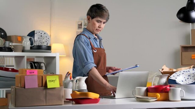 Mature Asian woman entrepreneur, Business owner working on laptop computer checking address and delivery detail before shipping product to client when working from home. Online selling business
