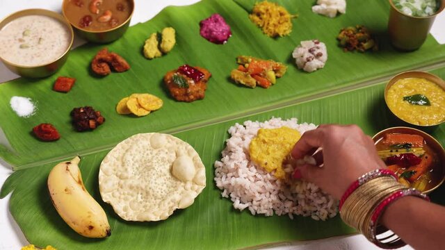 Woman eating traditional Onam sadhya with hand  4K footage video rice, Sambar, Rasam,  Avial,  Pappadom Payasam on banana leaf Onam Vishu Diwali festival vegetarian food Kerala South India.