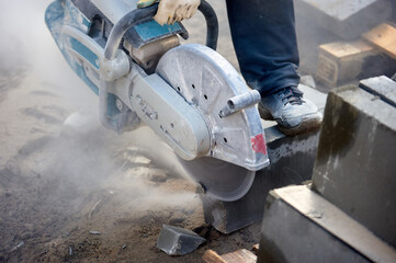 A worker with a circular saw cuts a curb stone close-up.