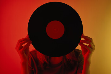 Woman hold retro vinyl disc in hands and covered her face, toned photo. Vintage style 80s and 90s...