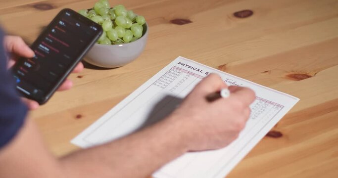 A young man writes weight, BMI, blood pressure, heart rate, and cholesterol on the paper by telephone records monthly, for the health check