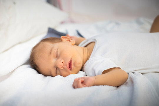Newborn sleeping lying on his back, on white and grey bedding. Side view.