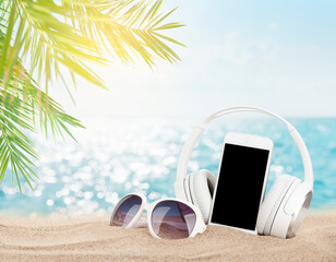 Smartphone, sunglasses and headphones on tropical sea beach