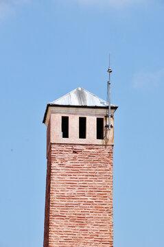 High brick tower with a lightning rod. Tower with a conical roof against a blue sky background.