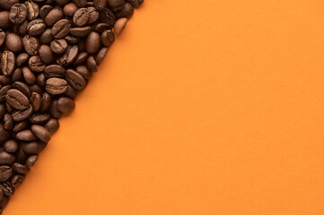 Roasted coffee beans on orange background with copy space. Close up top view.
