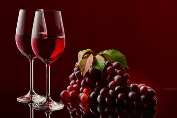 Two glasses of red wine and a bunch of grapes on a glossy table.