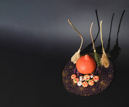 Witch&acute;s broomssticks, pumpkin and little fabric pumpinks standing on witch&acute;s hat. Funny Halloween minimal decoration concept on black background