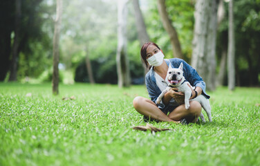 Naklejka na ściany i meble A woman wearing a medical mask sitting on the lawn with a white French bulldog.