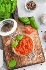 Traditional Italian marinara sauce in a jar on a concrete background with spices and ingredients. Top view. Copy space.