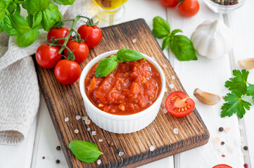Traditional Italian marinara sauce in a bowl on a white wooden background with spices and ingredients. Copy space.