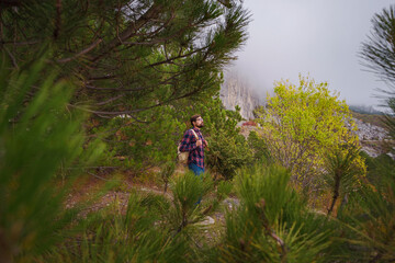 Obraz premium Male hipster Traveler with backpack in plaid shirt and jeans hiking in the mountains travel, trekking in autumn countryside. among the green pines
