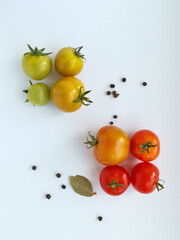 Green, yellow, red tomatoes and peppercorns on a white background. Top view