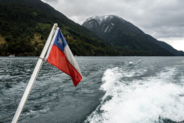 Chilean flag waving with in the Lago de Todos Los Santos and its snow-capped mountains in the background.
