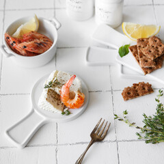 Shrimp on a white table serving for lunch, next to cheese and spices.