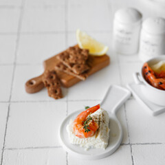 Shrimp on a white table serving for lunch, next to cheese and spices.
