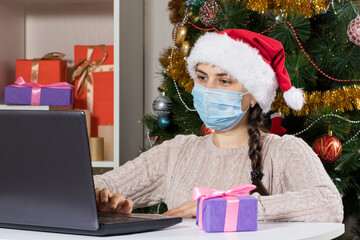 Shopping online gifts for Christmas and New Year. A woman sits near a laptop in a Santa Claus hat.