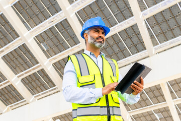 Ethnic contractor with tablet standing near solar power station