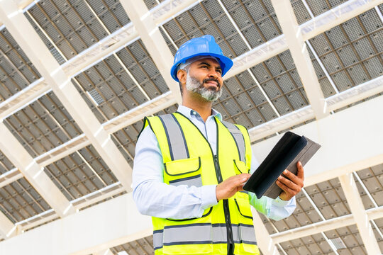 Ethnic contractor with tablet standing near solar power station