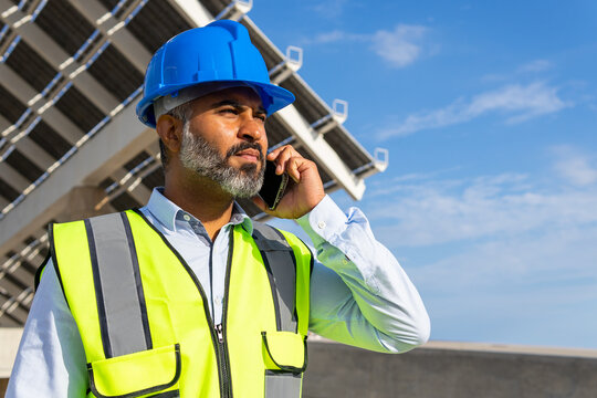 Ethnic supervisor in hardhat with smartphone against solar power station
