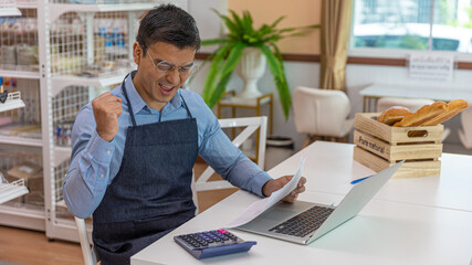Young male owner is checking his stocks and goods in his startup bakery or café shop at the end of the day with light flair from the window. Young entrepreneur working on his account and coming orders