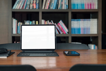 Blank screen laptop and gadget on wooden table in library room.