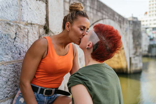 Happy lesbian couple kissing on urban embankment