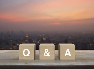 Q and A letter on block cubes on wooden table over blur of cityscape on warm light sundown,...