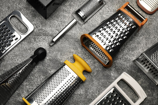 Different modern graters on grey table, flat lay