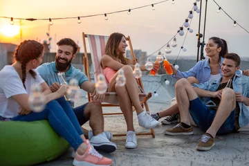 Foto op Plexiglas Gelukkige vrienden roosteren met drankjes op een feestje op het dak © NDABCREATIVITY